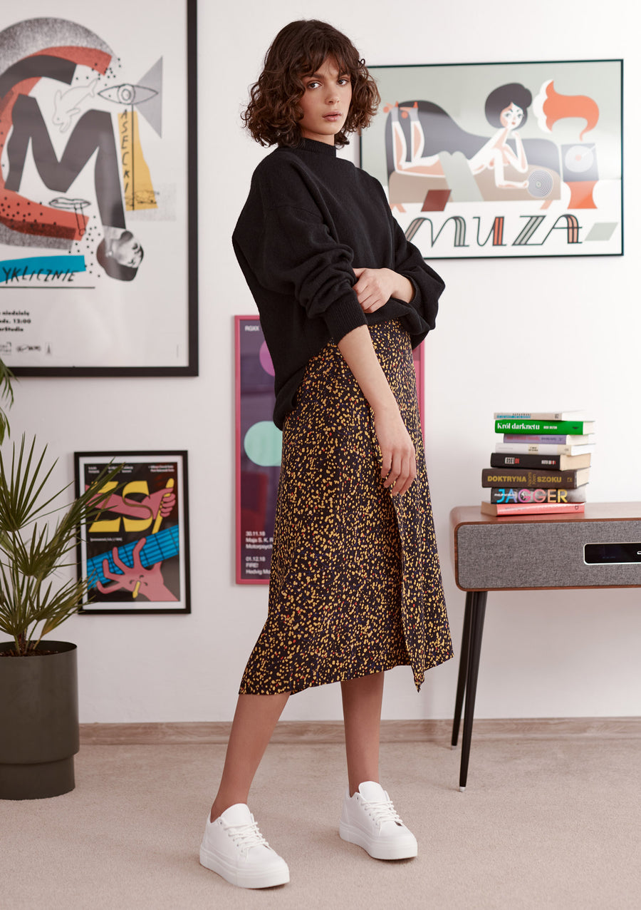 Black and yellow splatter print wrap skirt worn by a model. Styled with balck jumper and white trainers. Front