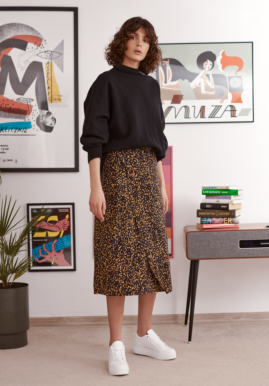 Black and yellow splatter print wrap skirt worn by a model. Styled with balck jumper and white trainers. Front