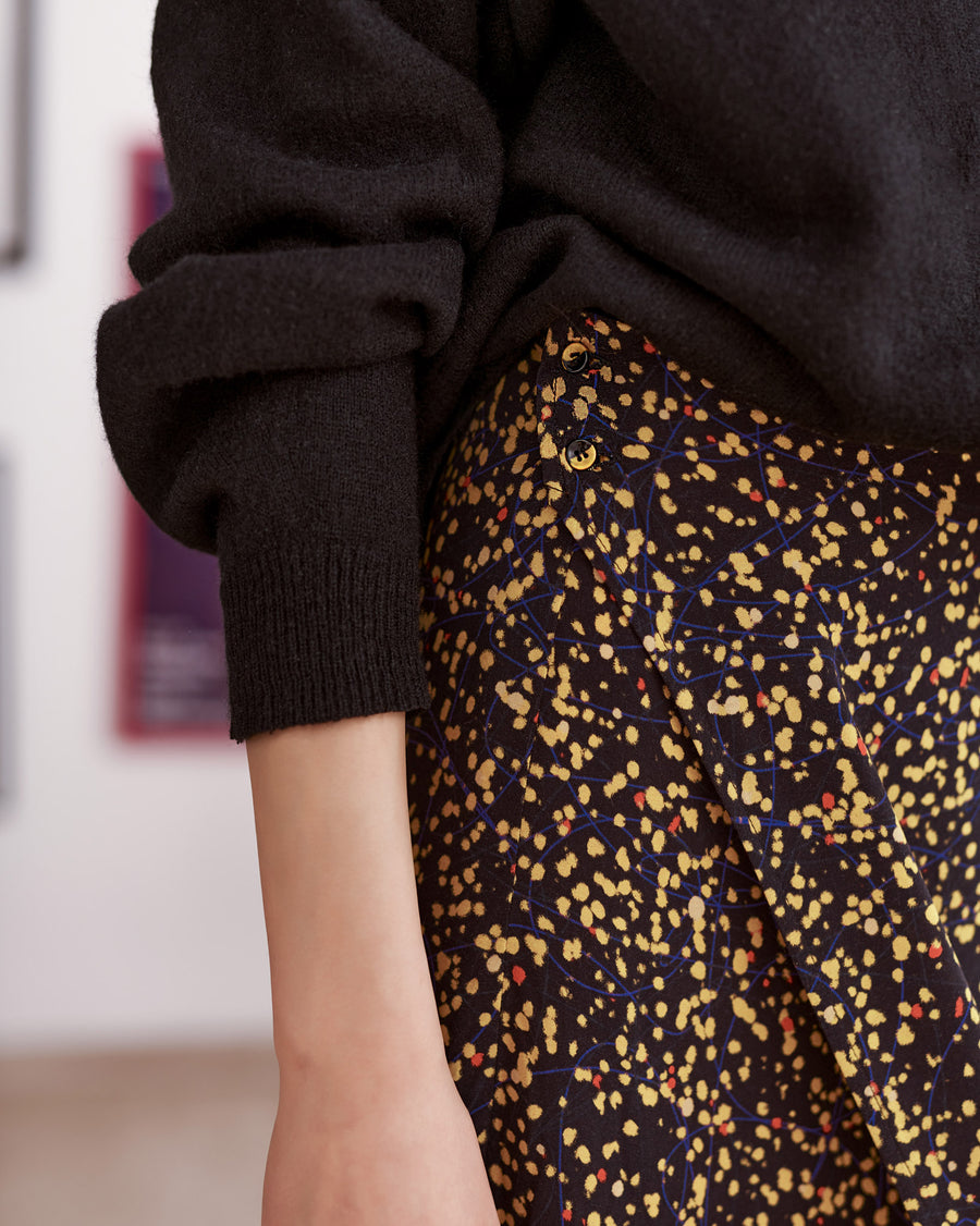 Black and yellow splatter print wrap skirt worn by a model.Buttons close up