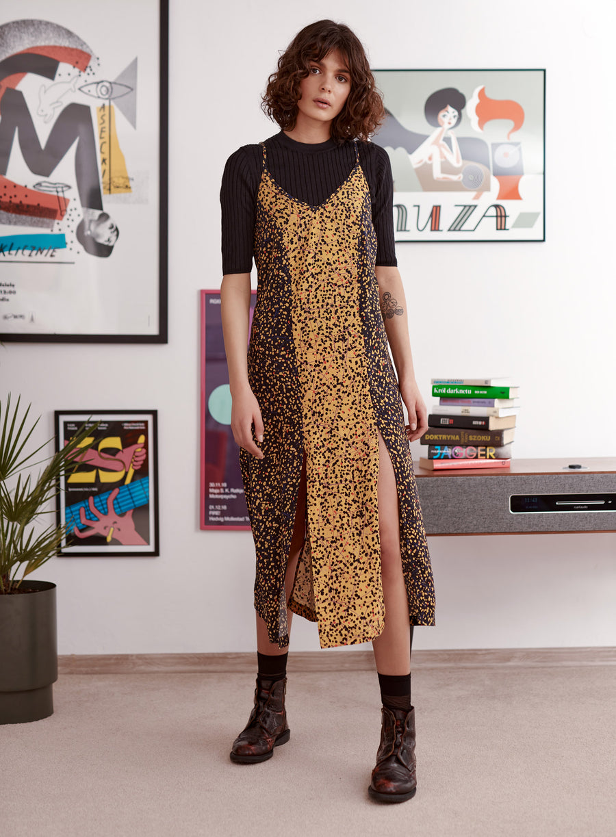 Black and yellow splatter print slip dress with splits at hem worn by a model. Styled with top, socks and heavy boots
