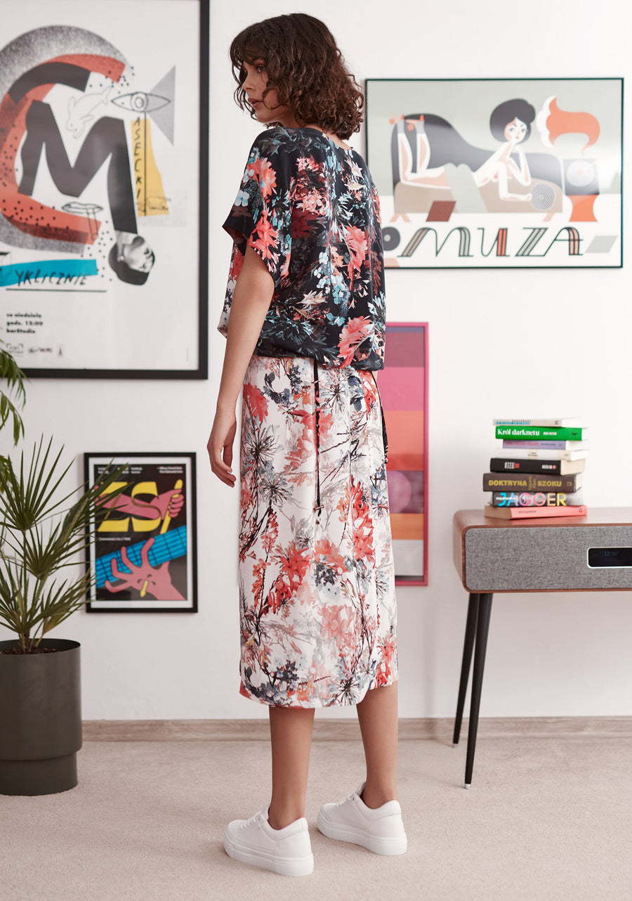 Red and blue floral print on white ground wrap skirt worn by model. Styled with matching printed top and white trainers. Back