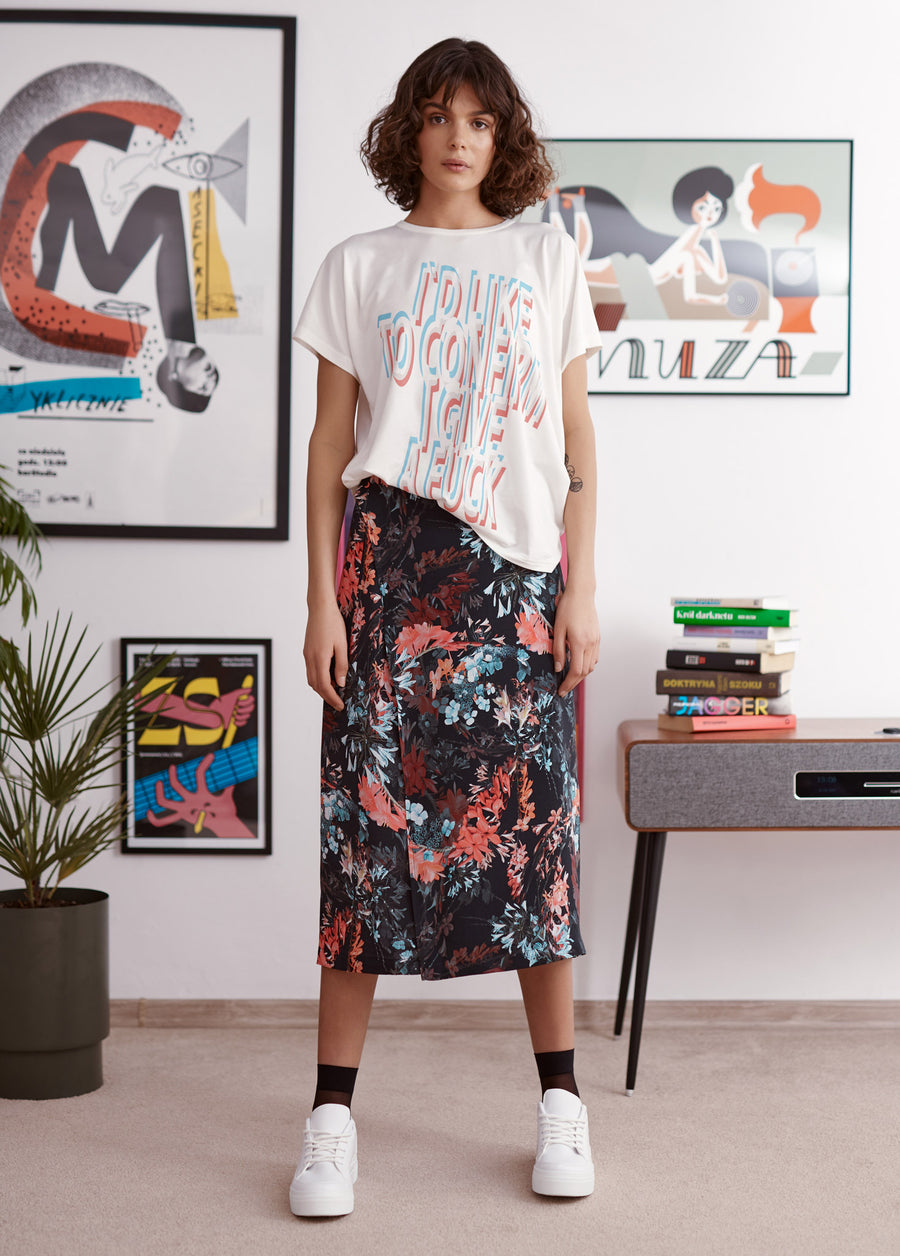 Blue and red statement slogan printed ivory t-shirt worn by a model. Styled with floral print skirt, black socks and white trainers.
