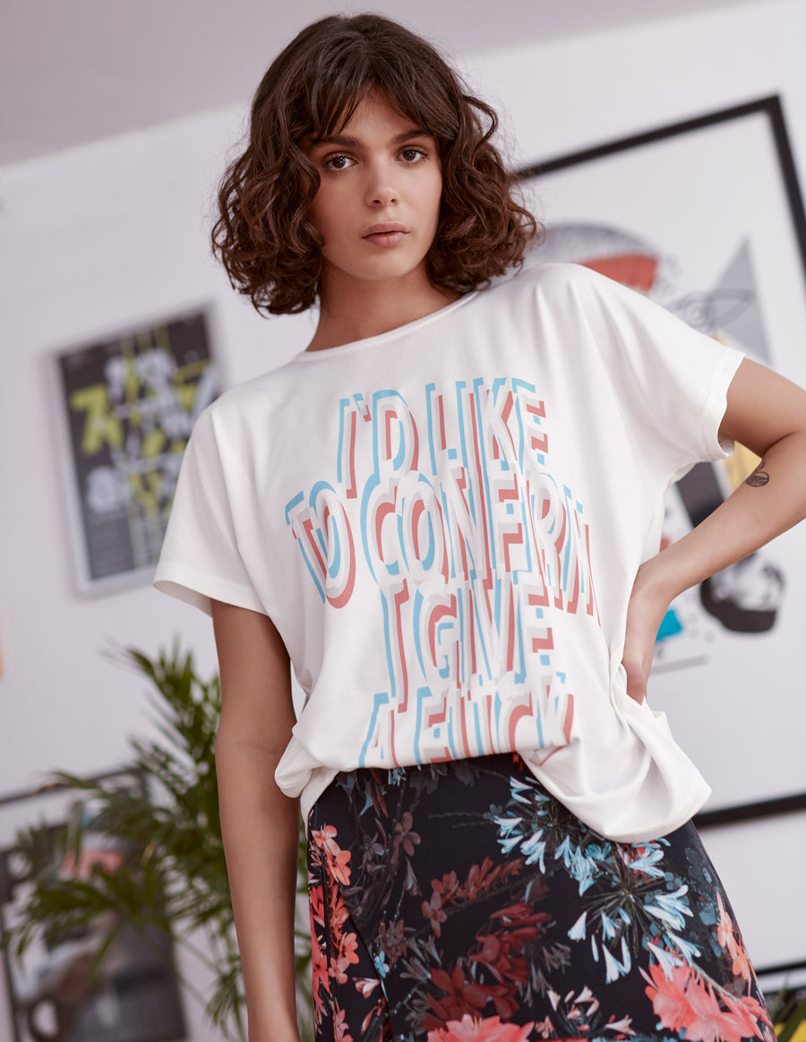 Blue and red statement slogan printed ivory t-shirt worn by a model. Styled with floral print skirt. Close up 