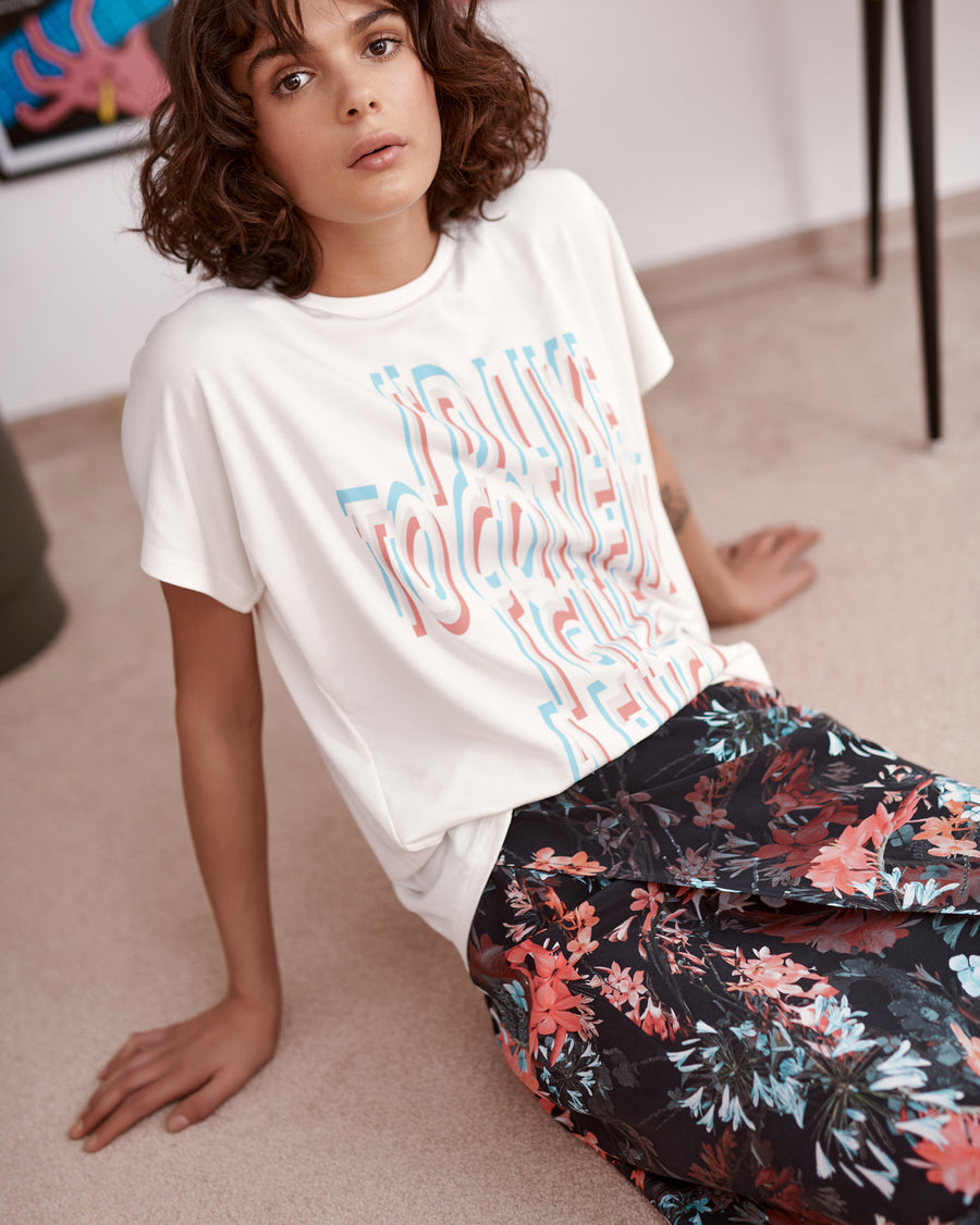 Red and blue floral print on black ground wrap skirt worn by model. Styled with slogan printed t-shirt. Close up.