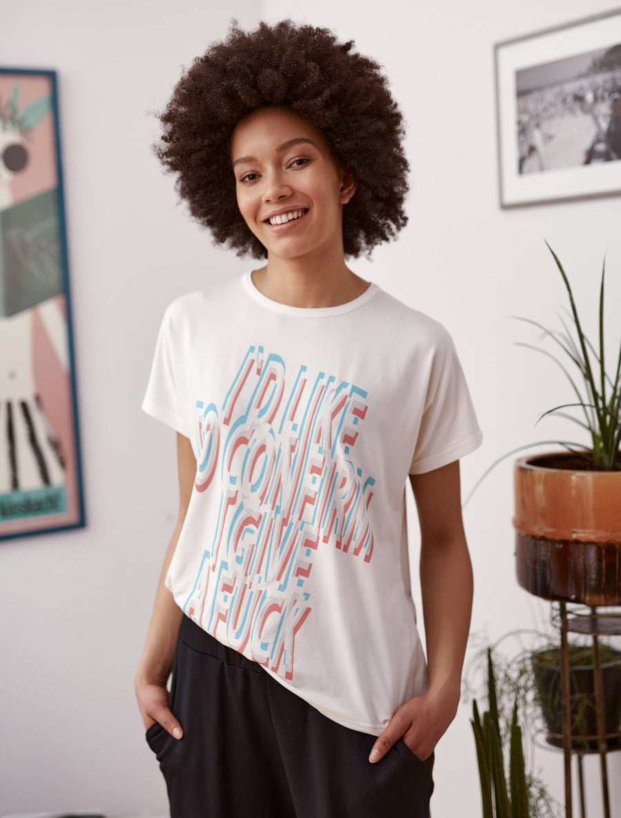 Blue and red statement slogan printed ivory t-shirt worn by a model. Styled with black joggers. Close up 
